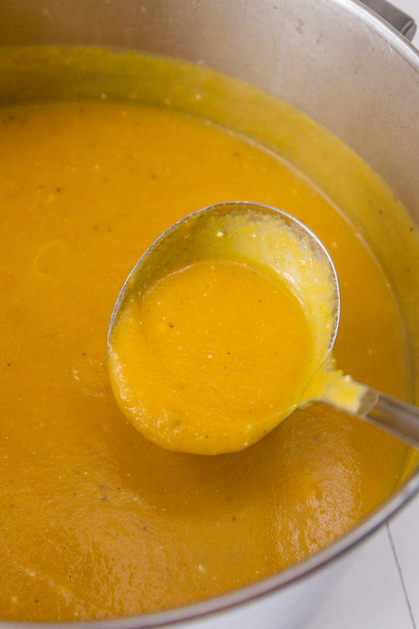 a pot full of carrot soup being ladled out