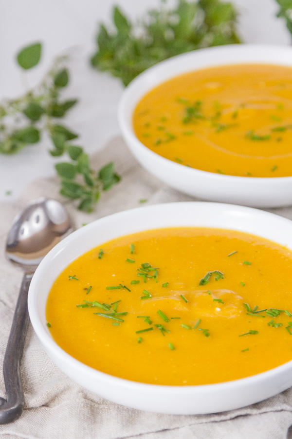 two bowls of carrot soup with a spoon and some fresh herbs