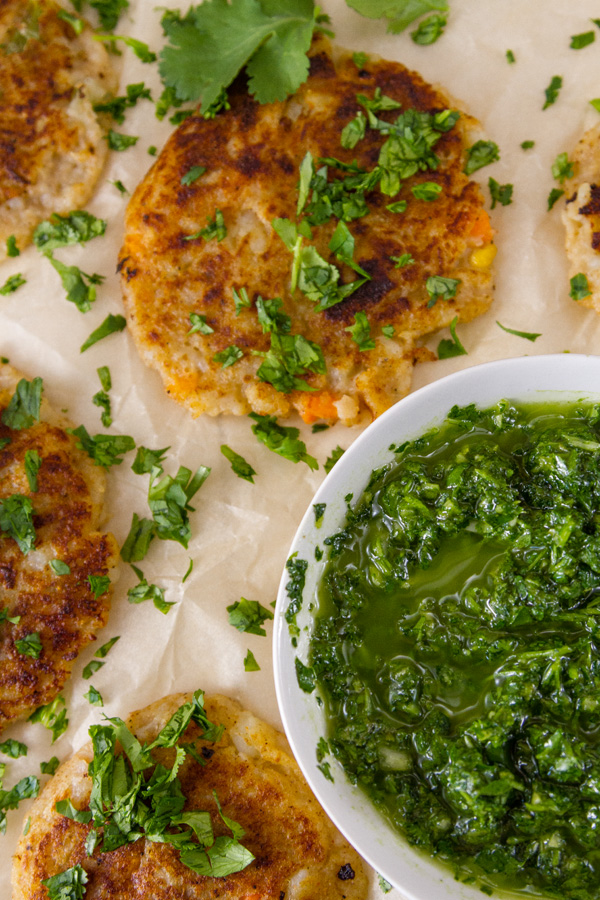 looking down on some cooked fritters served with green Chimichurri sauce, garnished with chopped cilantro.