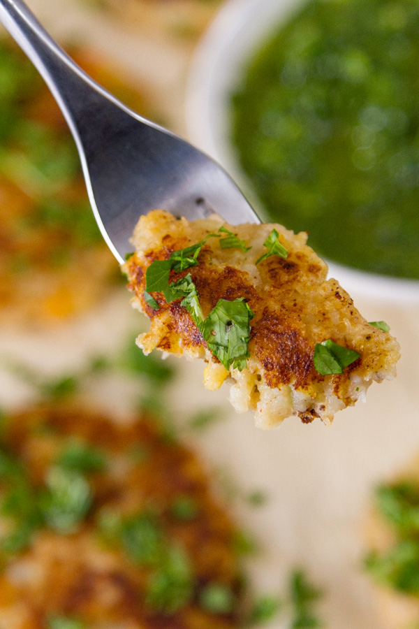 a fork full of a piece of potato fritter with more fritters and Chimichurri in the background