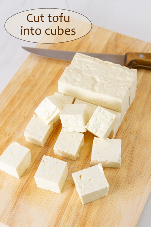 cutting tofu on a wooden cutting board with a knife.