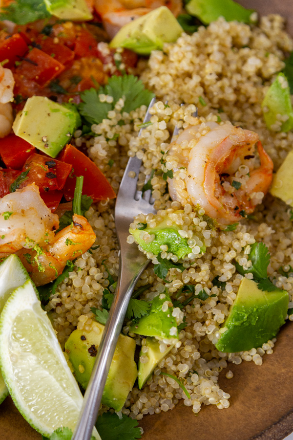 close up on fork in quinoa and shrimp bowl with veggies, served with lime wedges.