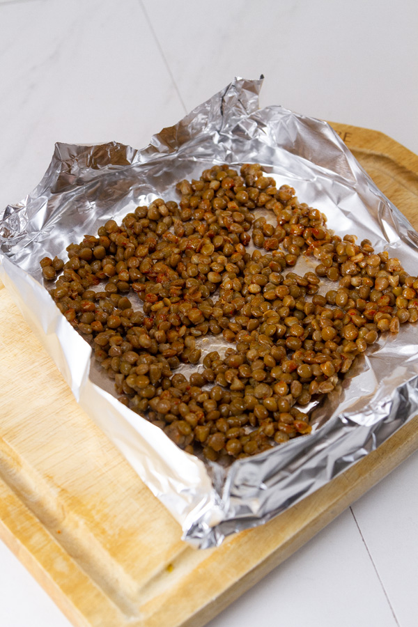 an aluminum foil tray filled with cooked lentils on a wooden cutting board.