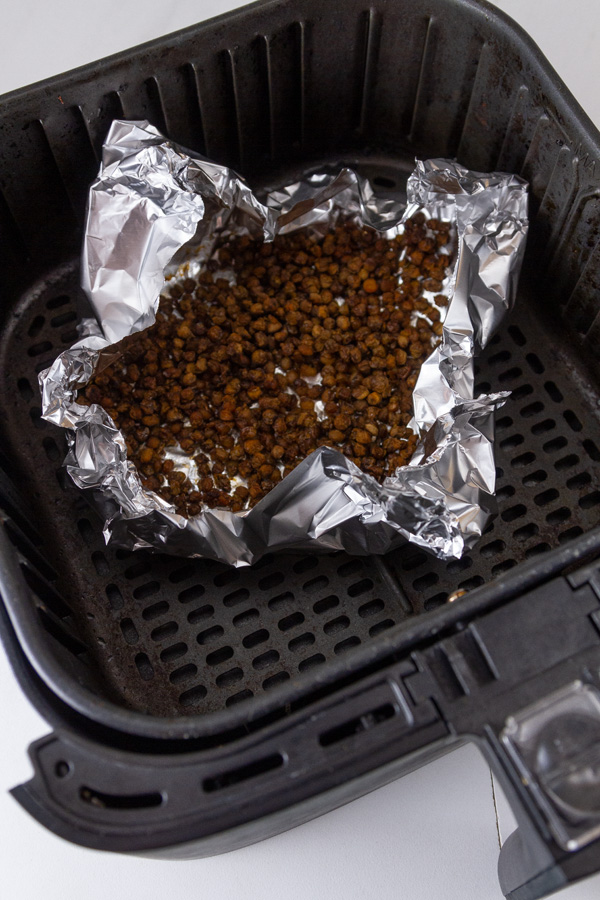 an aluminum foil tray with lentils inside in a drawer of an air fryer.