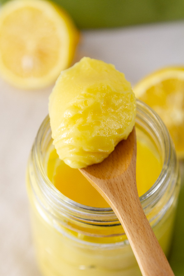 a spoonful of lemon custard on top of a jar that's surrounded by cut lemons.