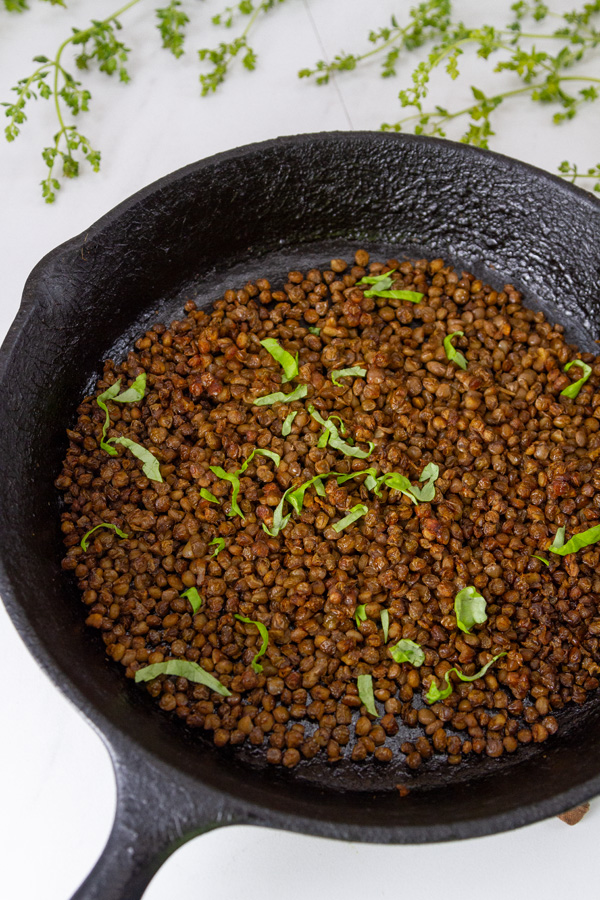 cooked lentils in a cast iron skillet garnished with chopped basil.