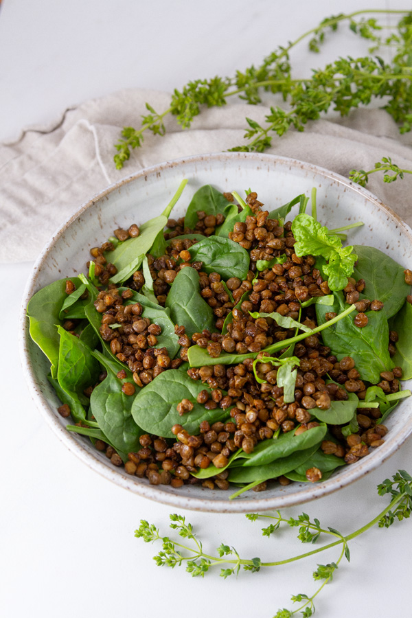 cooked lentils in a white bowl with fresh spinach leaves.