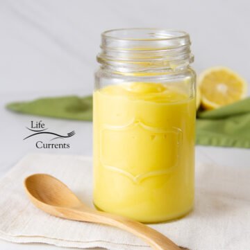 a jar of bright yellow custard with a wooden spoon, green napkin, and cut lemons.
