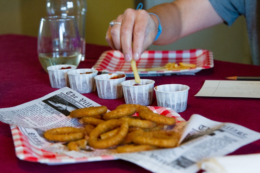 tasting ketchups in white paper cups, onions rings in front and French fries in the back.