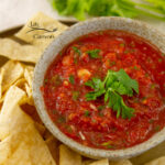 square crop of tomato salsa in a bowl garnished with cilantro and served with chips.