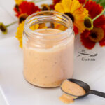 square crop of a jar filled with Comeback Sauce and a black spoon with the sauce on it, flowers in the background.