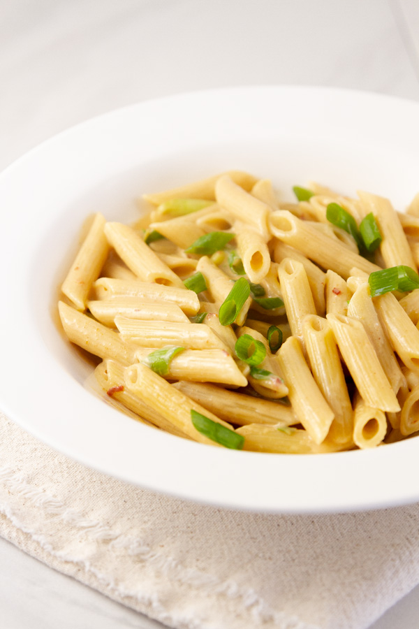 Creamy Peanut Noodles in a white bowl garnished with green onions.