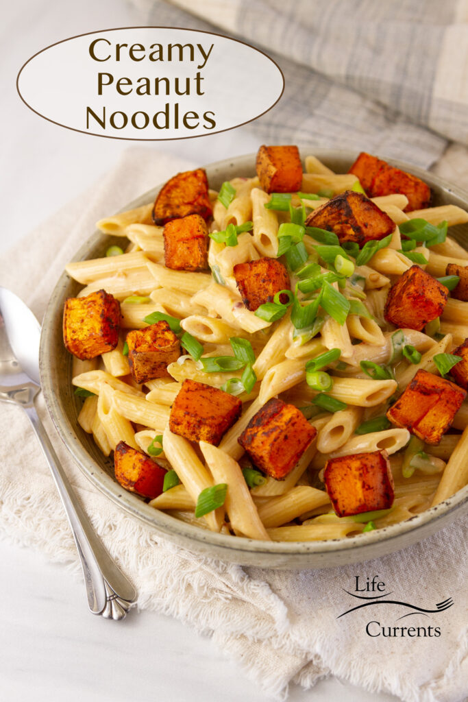 Creamy Peanut Noodles with roasted sweet potatoes and green onions in a bowl and a spoon is next to it, title on image.
