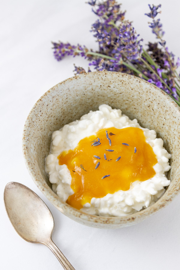 a bowl of cottage cheese topped with peach butter and lavender flowers, a spoon next to it, and more lavender in the background.