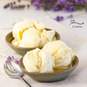 square crop of two bowls of ice cream with a spoon and lavender flowers.