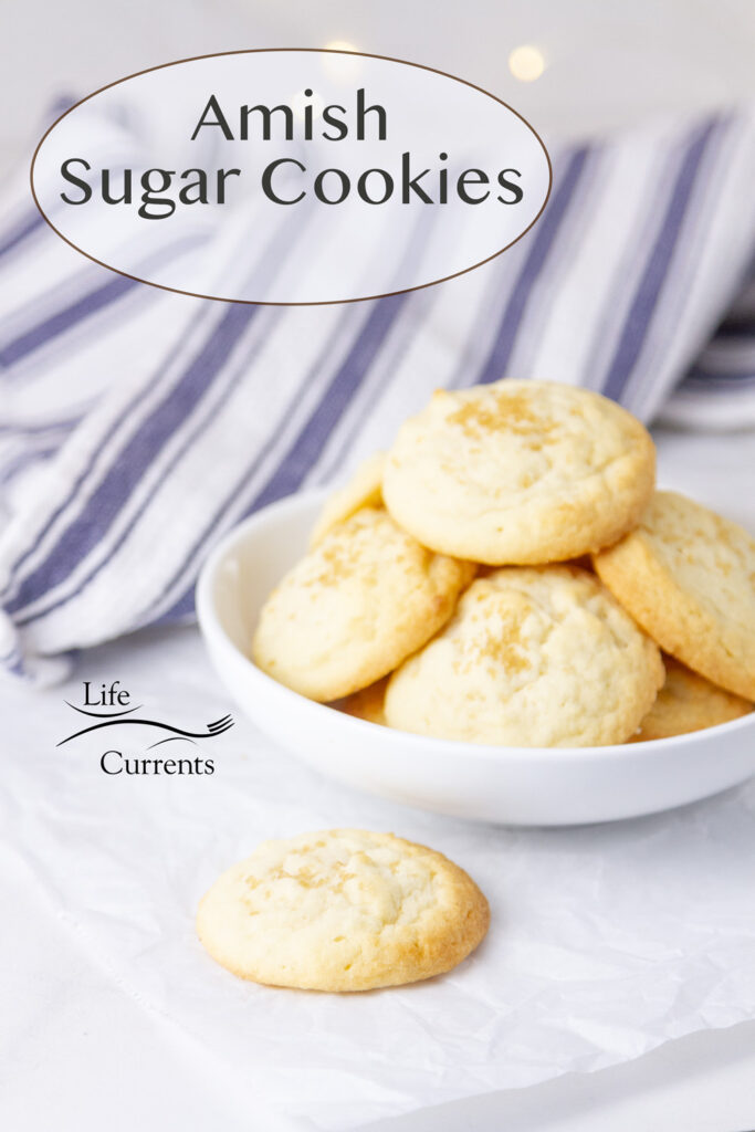 a bowl full of Amish Sugar Cookies with one next to the bowl, a blue and white striped towel in the background.