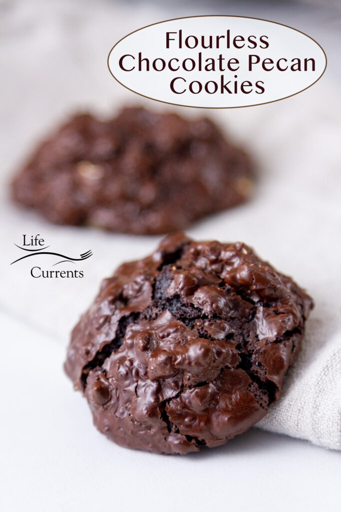 Two chocolate cookies on a cloth napkin, title on top right: Flourless Chocolate Pecan Cookies.