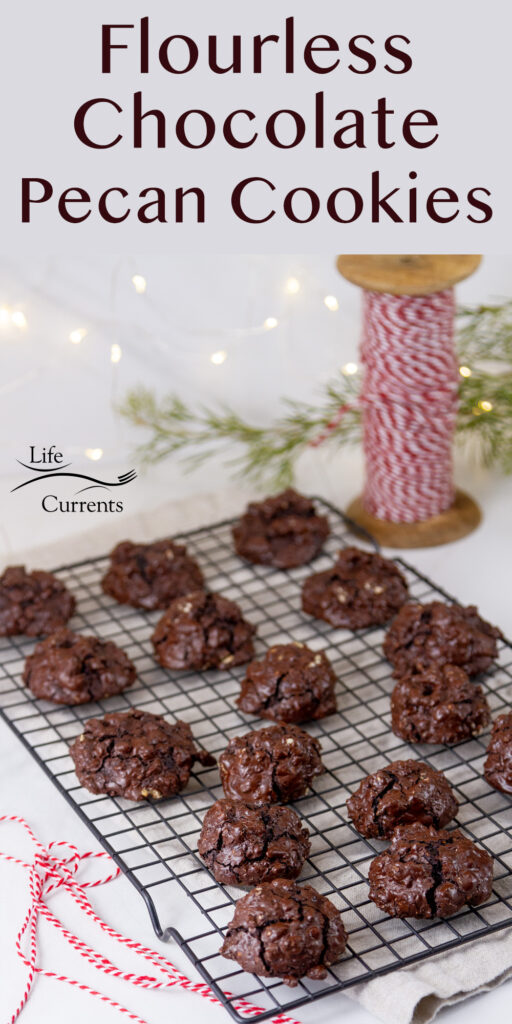 lots of Flourless Chocolate Pecan Cookies on a wire rack with Christmas lights, twine, and greenery around them.