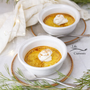 square crop of two cups of custard on plates with a cloth napkin and greenery around.