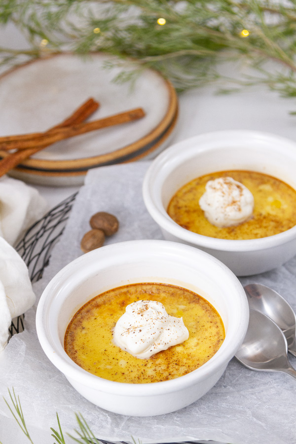 two custards in ramekins with spoons, plates, greenery, and spices around.