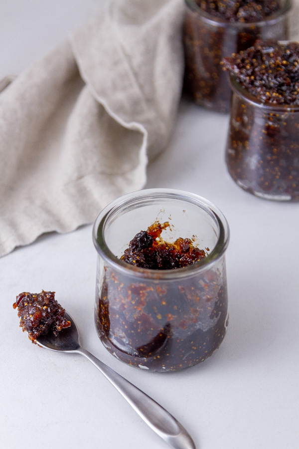 three glass jars filled with figs and a spoonful in front