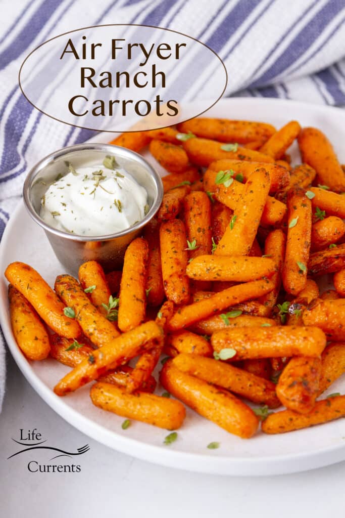 a white plate filled with cooked air fryer ranch carrots and a side dish or ranch dressing, a blue striped towel in the back.