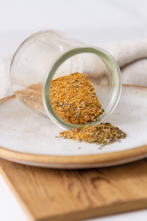 a glass jar of seasonings spilled on its side on a small plate.