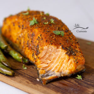 a piece of Air Fryer Cedar Plank Salmon on a cedar plank with herbs on top, and a bite taken out.