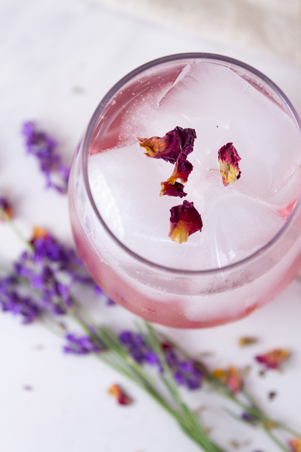 looking down into a glass filled with ice, cherry syrup, and soda, flowers garnishing and in front of the glass.
