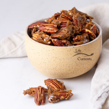 square crop of a bowl filled with candied pecans, some nuts have falled out of the bowl in the front.