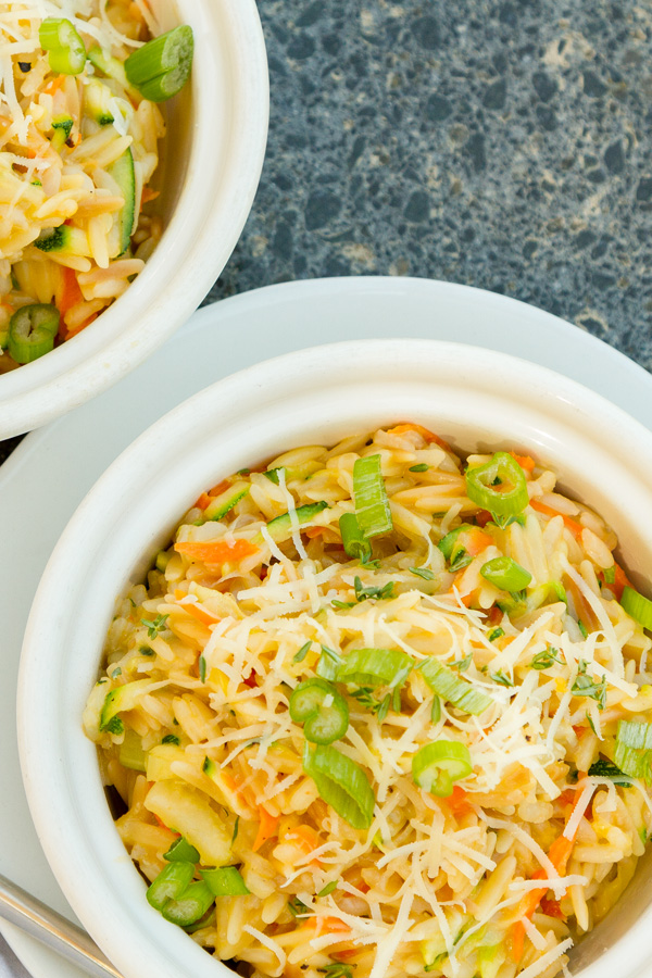Looking down into a bowl of veggies and pasta topped with cheese all on a granite background.
