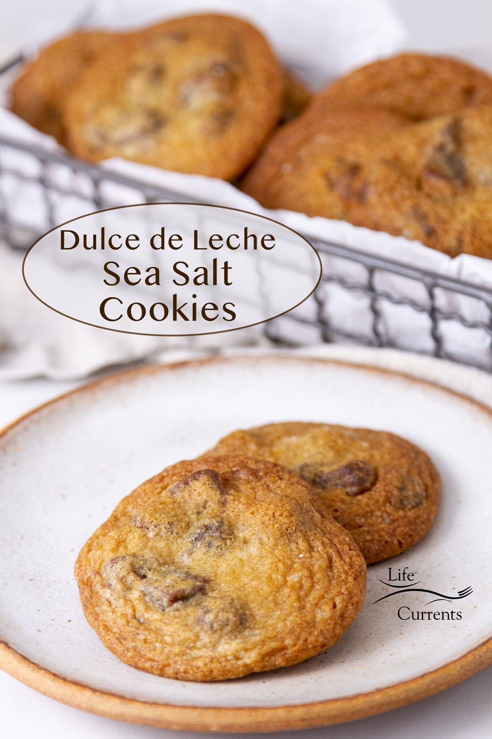 two cookies on a plate in front of a wire basket full of cookies, title on left: Dulce de Leche Sea Salt Cookies.