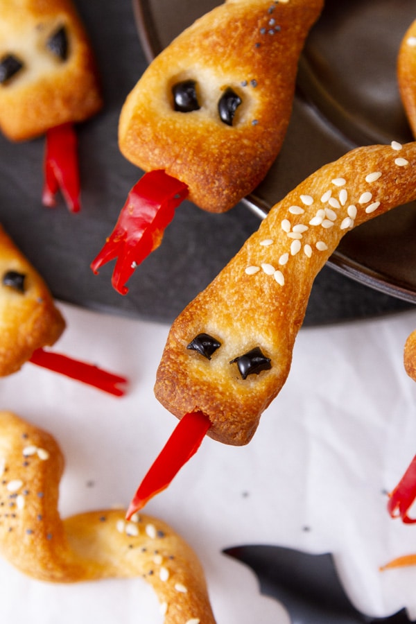 close up on bread snakes faces with black olives for eyes and red peppers for tongues.