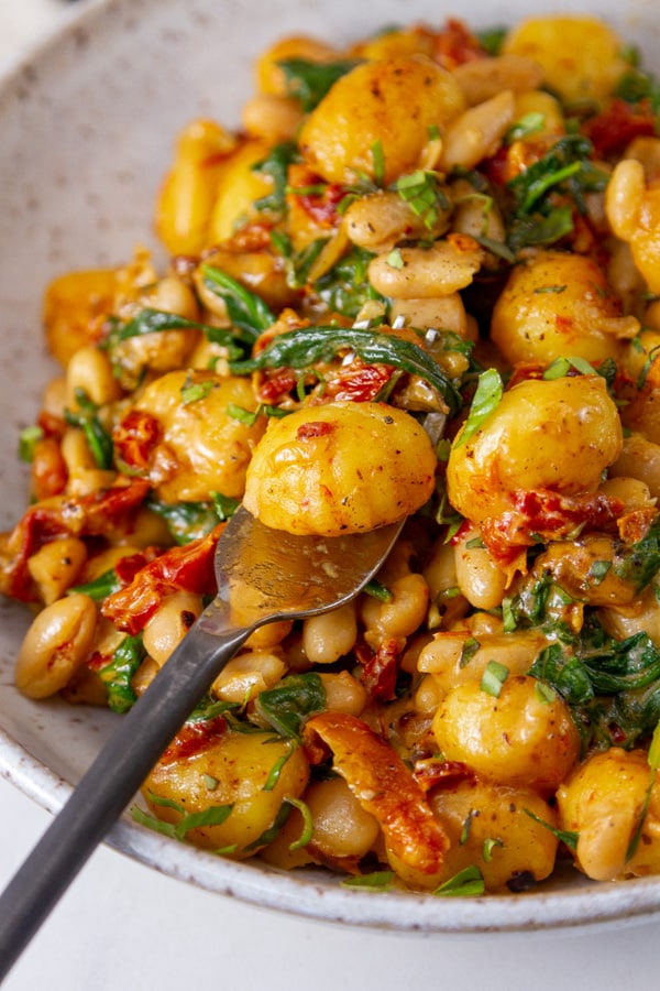 a fork with a gnocchi on it, in a pan with the rest of the meal.