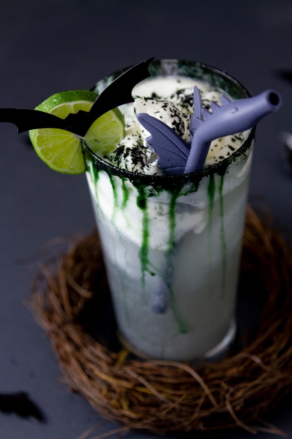 a cocktail drink with creamy topping, a lime wheel, a bat, and a dragon straw.