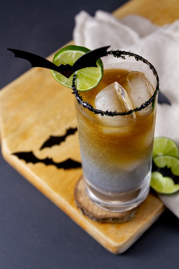 looking down on a cocktail drink in a glass with a lime wheel and a paper bat.