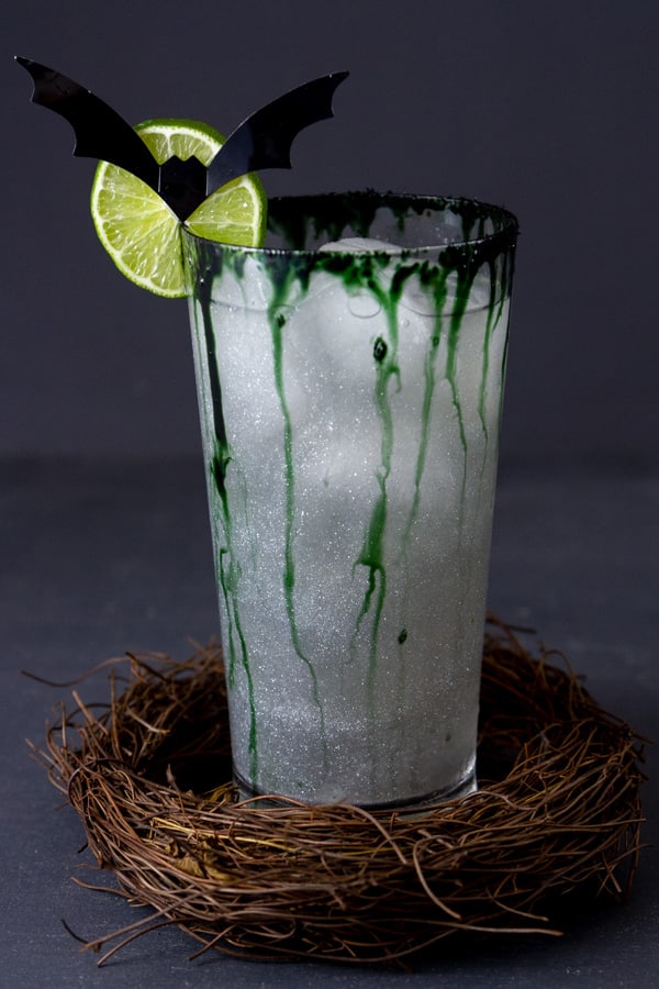 a virgin dark and stormy mocktail with lime wheel and bat garnish in a stick wreath.