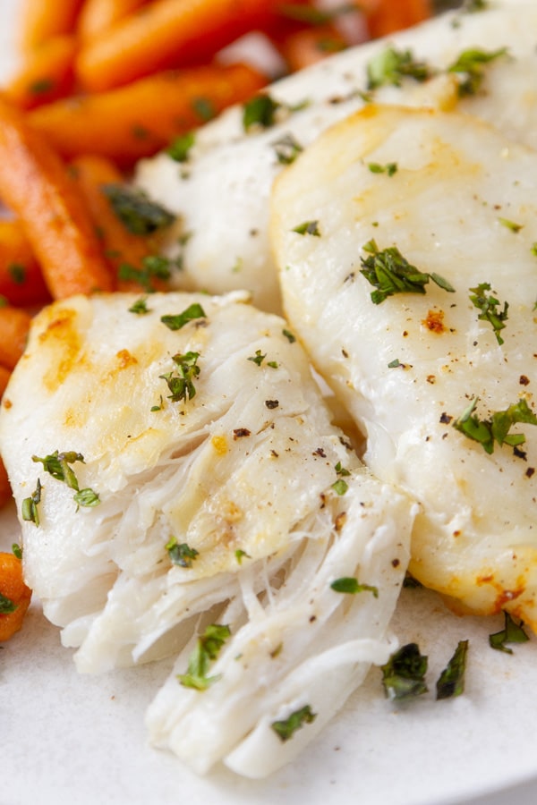 cooked hailbut cheeks with fresh herbs broken apart so you can see the flaky texture.