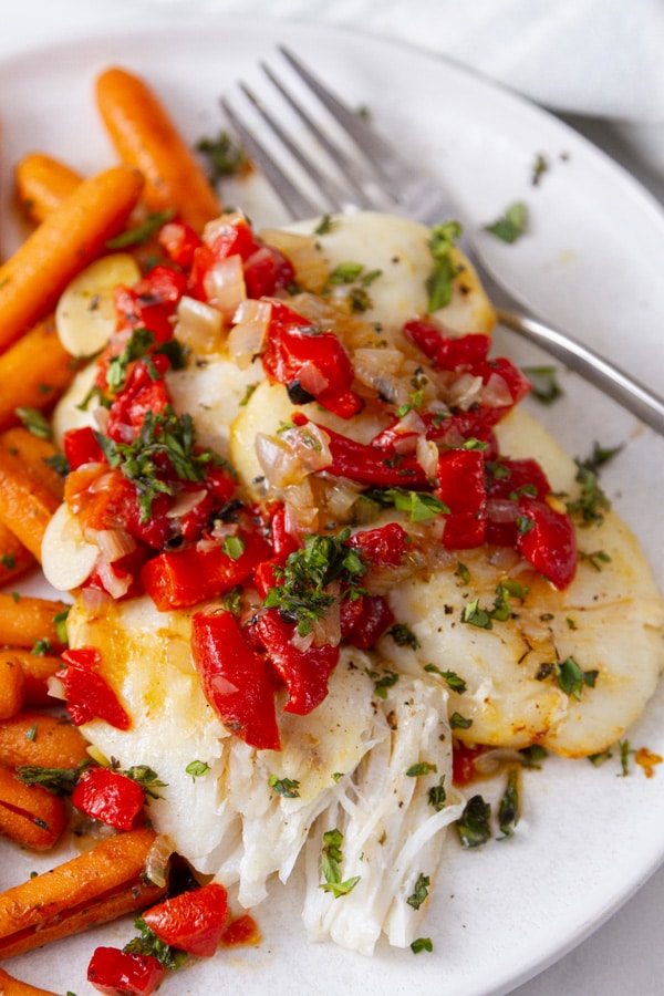 cooked halibut cheeks with red pepper shallot sauce and cooked carrots and a fork.