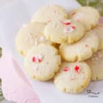 little sugar cookies topped with crushed peppermint sugar grouped on a piece of parchment paper on a pink serving tray with Christmas greens behind them.