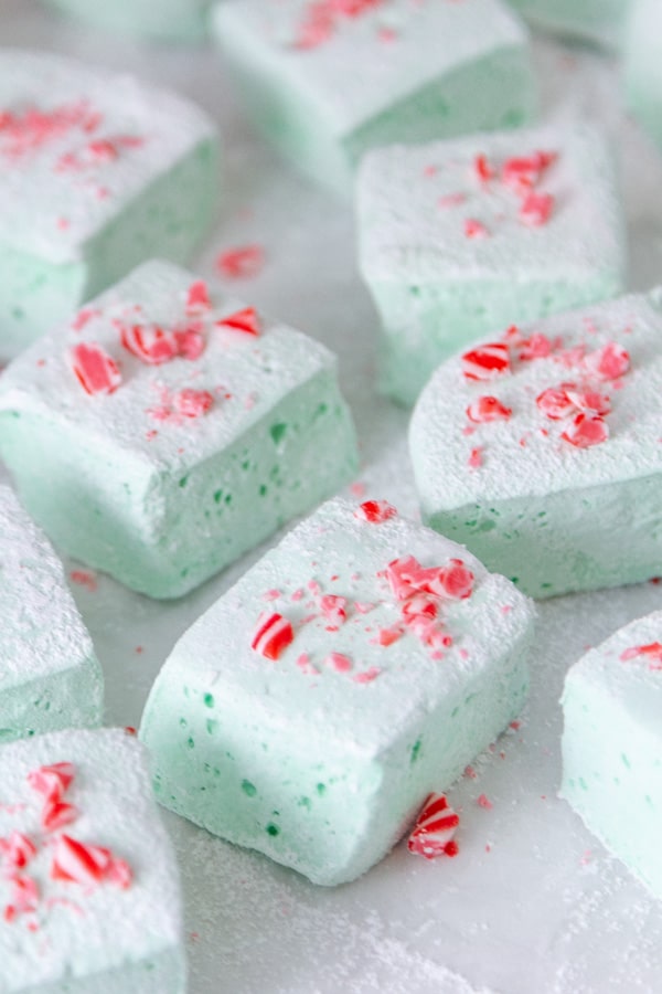 a bunch on square cut homemade green marshmallows on parchment paper garnished with crushed peppermints.