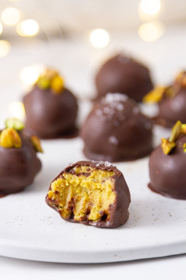 chocolate candies on a plate, one has a bite taken out so you can see the pistachio filling.