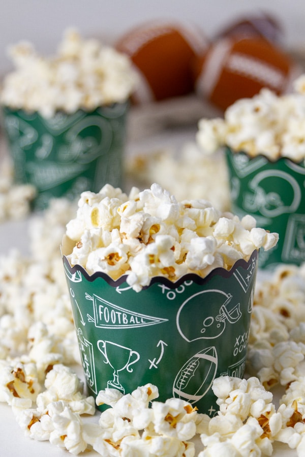 three green paper cups holding popped popcorn, some small footballs in the background.