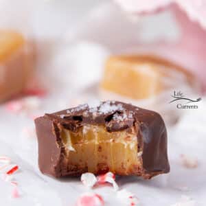 a chocolate dipped caramel that has a bite taken out of it, with some crushed peppermints around it.
