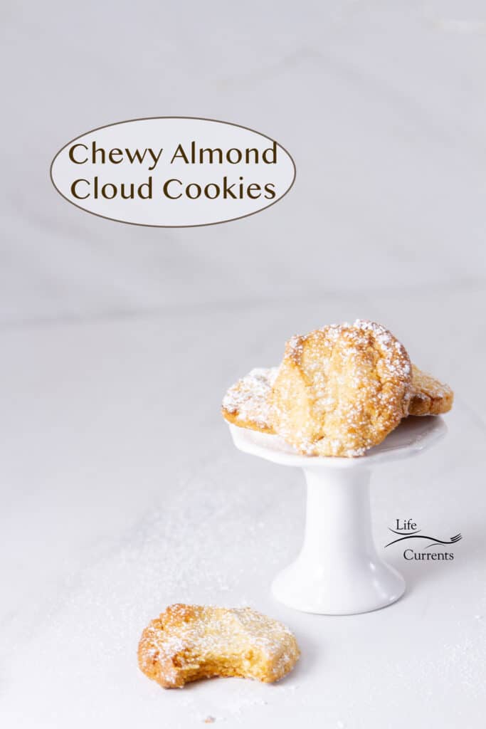 Chewy Almond Cloud Cookies on a white pedestal and one in front on the table with a bite taken out of it.