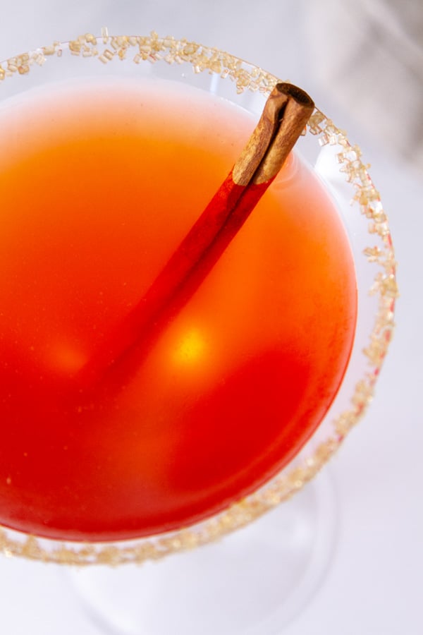 Looking down ingto a martini glass filled with cinnamon apple cider cocktail and a cinnamon stick and sugared rim garnish.