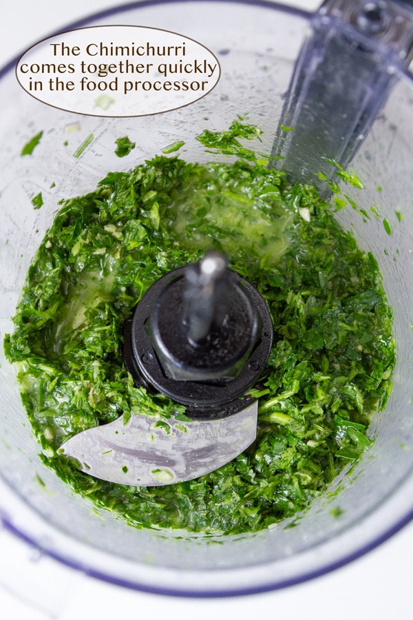 Looking into the bowl of a food processor filled with green chimichurri sauce.