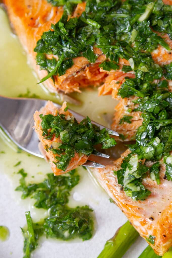 a bite on a fork taken out of a piece of cooked salmon with chimichurri on top.