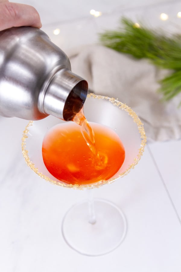 pouring apple cider cocktail from a shaker into a martini glass.