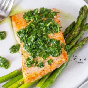 square crop of a piece of salmon with chimichurri sauce on top next to cooked asparagus.